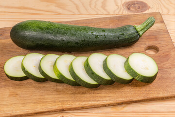 Whole and sliced dark green zucchini on the cutting board