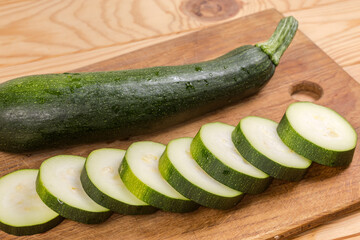 Whole and sliced dark green zucchini on the cutting board
