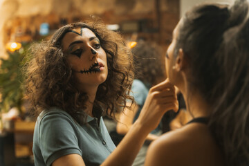 Naklejka premium Halloween party preparations, female friends checking face paint for costume