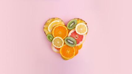 Fruit heart made of pineapple, grapefruit, orange, lemon and kiwi slices against pastel pink background. Copy space. Creative summer idea. Minimal fruit concept.