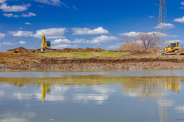 Excavator and earthmover are leveling ground over river