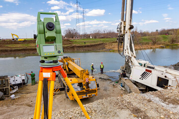 Total station in front of Mobile crane and drilling machine working together on bridge foundation