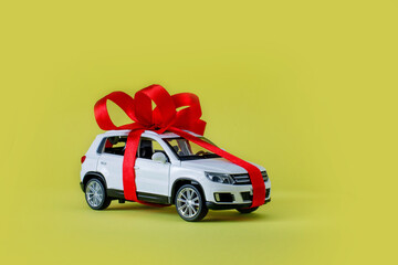White model car with bow on a yellow background. Car as gift, surprise