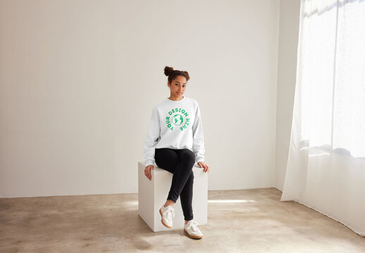 Mockup of woman wearing sweatshirt with customizable color sitting on plinth, full length