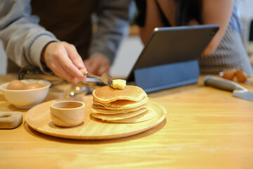 Young man preparing pancakes for breakfast putting butter on the hot pancakes