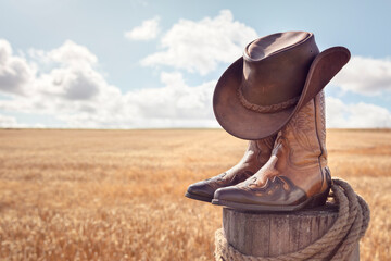 Cowboy hat, boots and wheat field background at ranch stables, country music festival live concert...