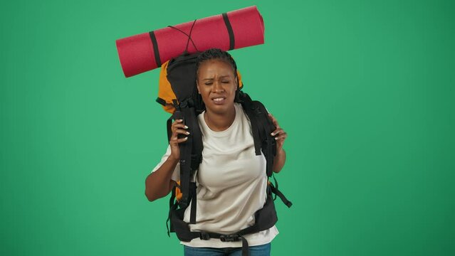 Woman tourist with heavy backpack looking very tired and sad. Isolated on green background.