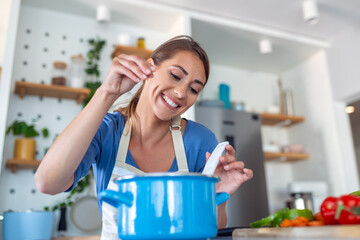 Joyful Young Lady Cooking and Sampling Dinner in a Pot, Present in a Contemporary Home Kitchen....