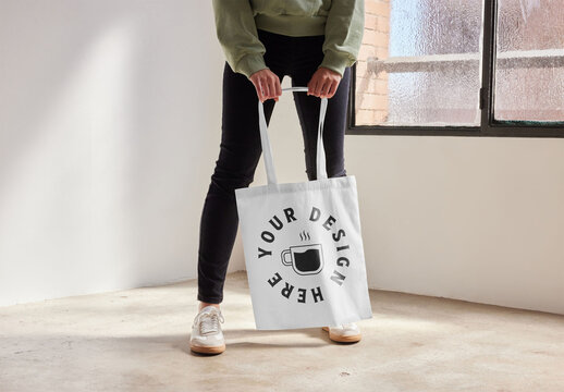 Mockup of woman standing holding customizable tote bag, low section