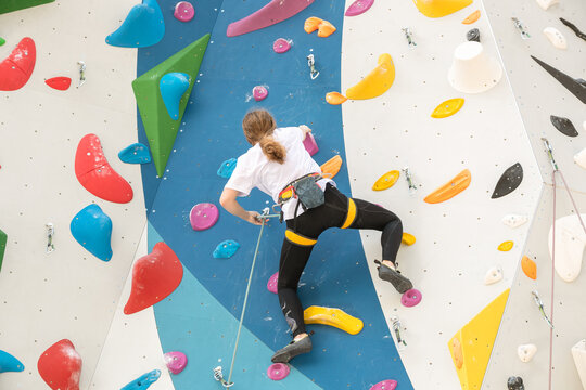 The climber climbs the artificial stone wall with the help of safety belts. An active young woman on a stone wall in a sports center. A girl trains on a rock climber in the open air. A beautiful, athl