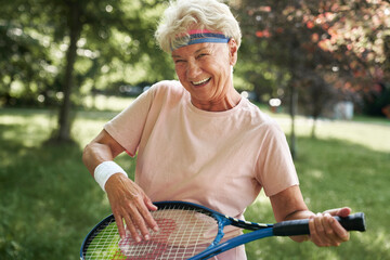 Portrait of senior woman standing in the park and holding tennis racket