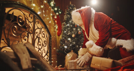 Authentic santa clause leaving christmas gifts near fireplace and christmas tree - chritmas spirit,...