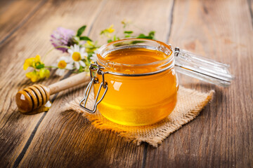Glass jar with floral liquid honey, flowers and honey dipper. Copy space