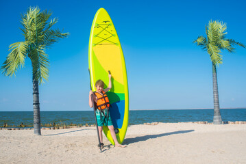 happy 10 year old boy holding a green sup board and paddle for sap boarding on a sunny day at the...
