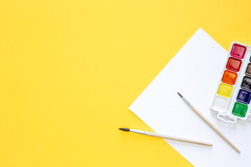Watercolor and brushes on a yellow background, flat lay, copy space.