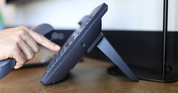 Call center and customer support. Operator hand trying to answer customer call using VoIP landline phone at help desk in office. Phone in hotel room