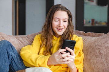 Fototapeta na wymiar happy teenage girl looks at phone screen at home