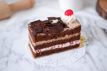 Chocolate cake with whipped cream and cherries on white marble background