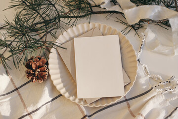 Calm Christmas still life. Blank greeting card, invitation mockup in sunlight. Plate, pine cone and...