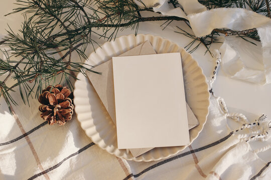 Calm Christmas Still Life. Blank Greeting Card, Invitation Mockup In Sunlight. Plate, Pine Cone And Pine Tree Branches On White Table Background. Checkered Plaid. Cozy Winter Scene. Flatlay, Top View