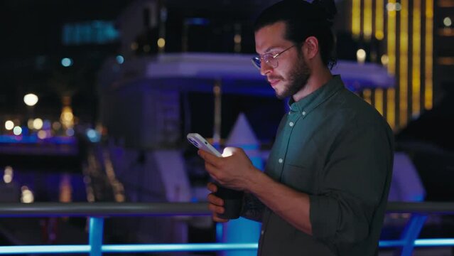 Handsome Happy Guy Using Smartphone While Walking on Night City Street.