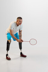 Full length of confident man with prosthesis play badminton, ready to serve from opponent against white studio background.