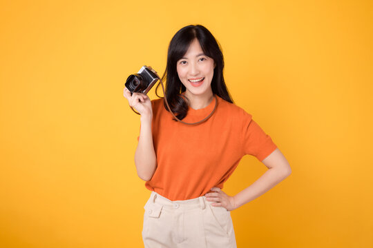 Young asian woman 30s with camera, ready for a fun adventure tour. Positive holiday vibes on a yellow background.
