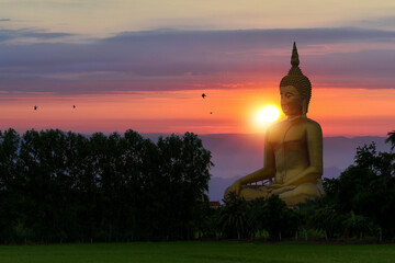 Large golden Buddha statue in Wat Muang, Ang Thong Province, Thailand, against a sunset or sunrise backdrop.