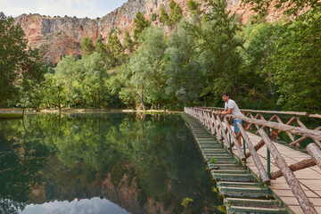 Man standing on a footbridge by a lake