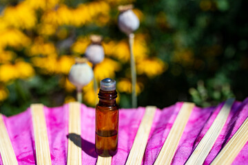 Essential oil bottle roll on on a pink folding fan with flowers and poppy buds in the background