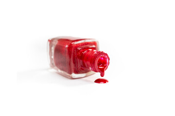 Opened bottle with bright red nail polish spilling isolated on white