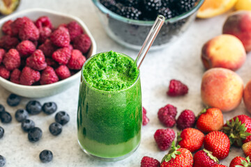 Glass of green smoothie on blurred kitchen table with berries.
