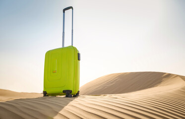 Fototapeta na wymiar bright light green or yellow suitcase in sands of desert dunes. Concept and idea of travel to United Arab Emirates, Dubai sands at sunset. Summer holiday travel concept