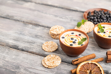 Yoghurt with bilberry and caramel in clay bowl on gray wooden, side view, copy space.