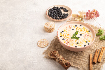 Obraz na płótnie Canvas Yoghurt with bilberry and caramel in ceramic bowl on gray concrete, side view, copy space.