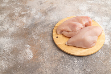 Raw chicken breast on brown concrete background. Side view, copy space.