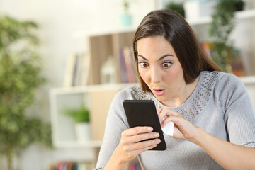 Surprised woman cleaning smart phone at home