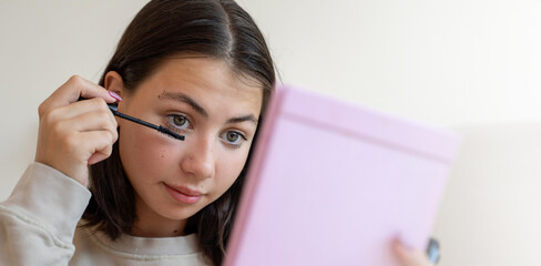 Teenage girl putting makeup. Young woman looking at mirror and apply mascara on eyelashes in...