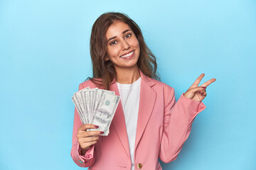 Teen girl in pink, flaunting a handful of dollar bills joyful and carefree showing a peace symbol...