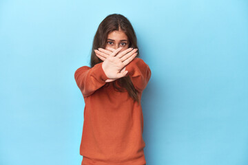 Teen girl in vibrant orange sweater on blue doing a denial gesture