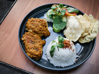 Ayam bakar Taliwang is a traditional roast chicken from Lombok Indonesia, isolated on a wooden background, served with vegetables. Spicy but tasty cuisine