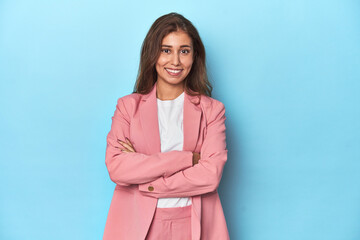 Teen girl in chic pink suit on a blue background who feels confident, crossing arms with determination.