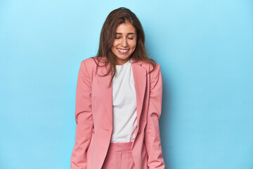 Obraz premium Teen girl in chic pink suit on a blue background laughs and closes eyes, feels relaxed and happy.