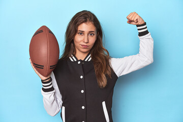 Young woman in baseball jacket with football ball in studio.