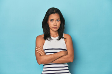Filipina young woman on blue studio suspicious, uncertain, examining you.
