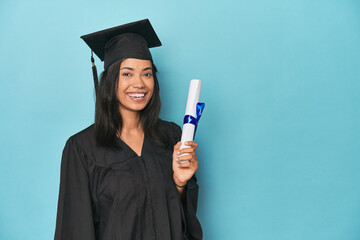 Celebrating Filipina graduate with diploma and cap on blue studio