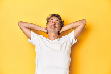 Fototapeta na wymiar Middle-aged man posing on a yellow backdrop feeling confident, with hands behind the head.