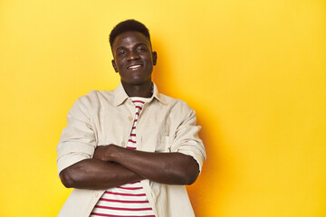 Stylish young African man on vibrant yellow studio background, smiling confident with crossed arms.