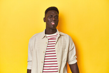 Stylish young African man on vibrant yellow studio background, funny and friendly sticking out tongue.