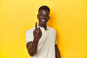 Stylish young African man on vibrant yellow studio background, pointing with finger at you as if inviting come closer.